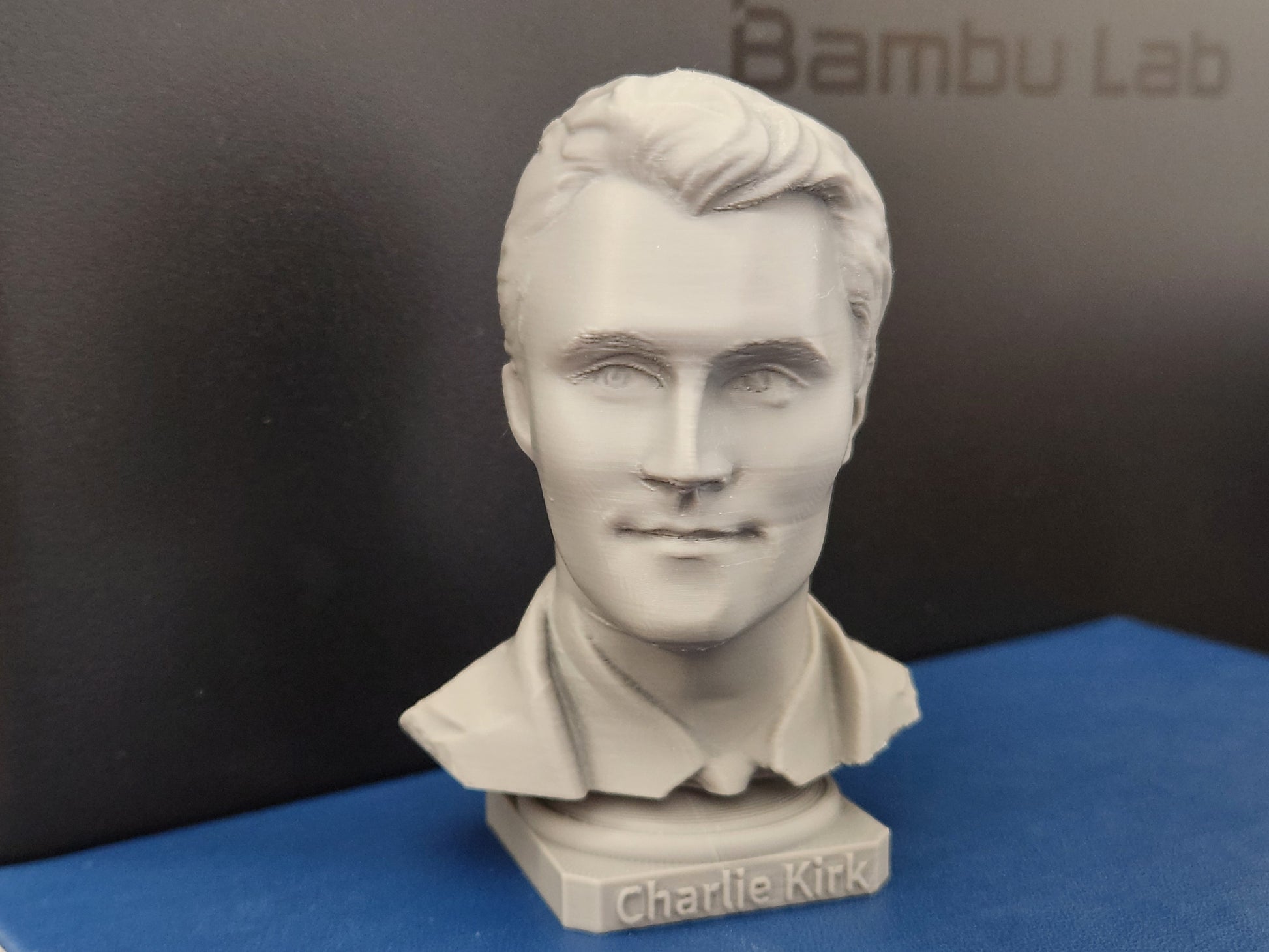 3D printed bust sculpture of Charlie Kirk in light gray with detailed facial features and engraved base