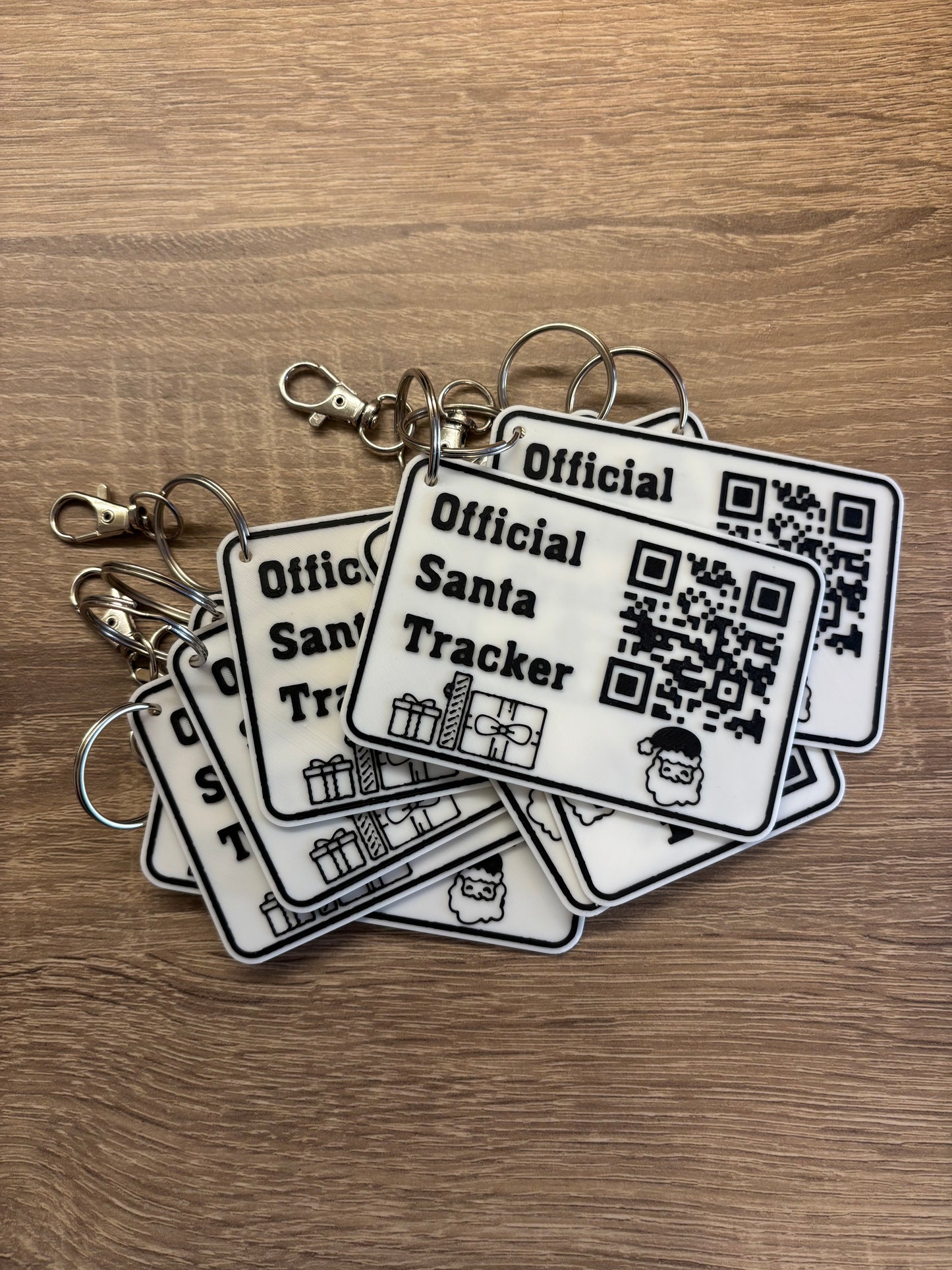 Stack of official Santa Tracker keychains with QR codes on wooden surface