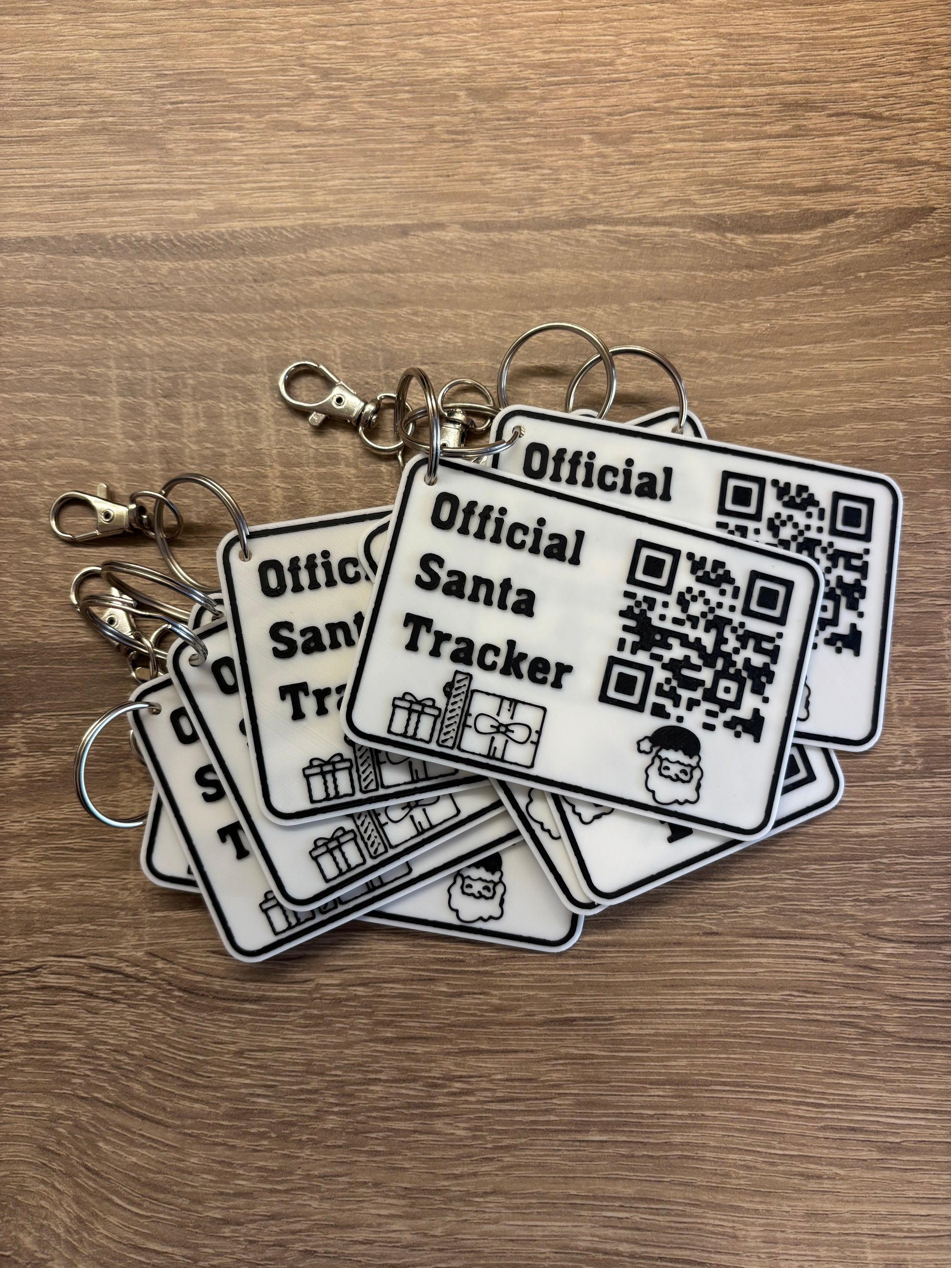 Stack of official Santa Tracker keychains with QR codes on wooden surface