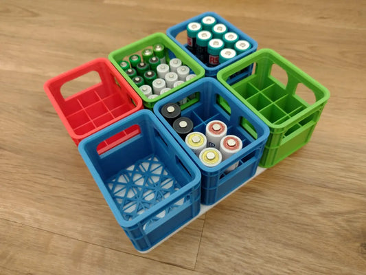 Set of colorful 3D printed battery crates holding various batteries on wooden surface