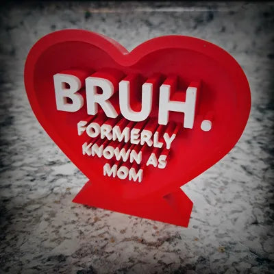 Red 3D printed heart with white text 'BRUH. FORMERLY KNOWN AS MOM' on gray surface