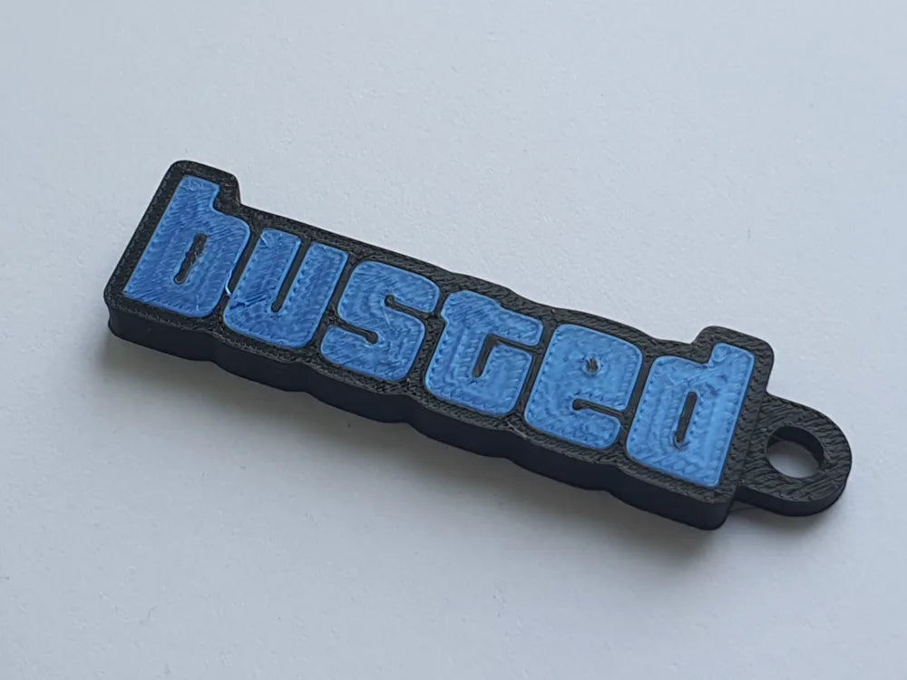 3D printed 'busted' keychain with blue letters and black border