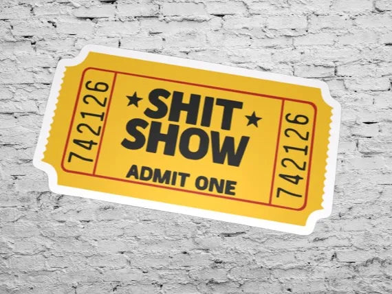 Yellow ticket-shaped sticker with bold black text 'SHIT SHOW ADMIT ONE' on a brick wall background.