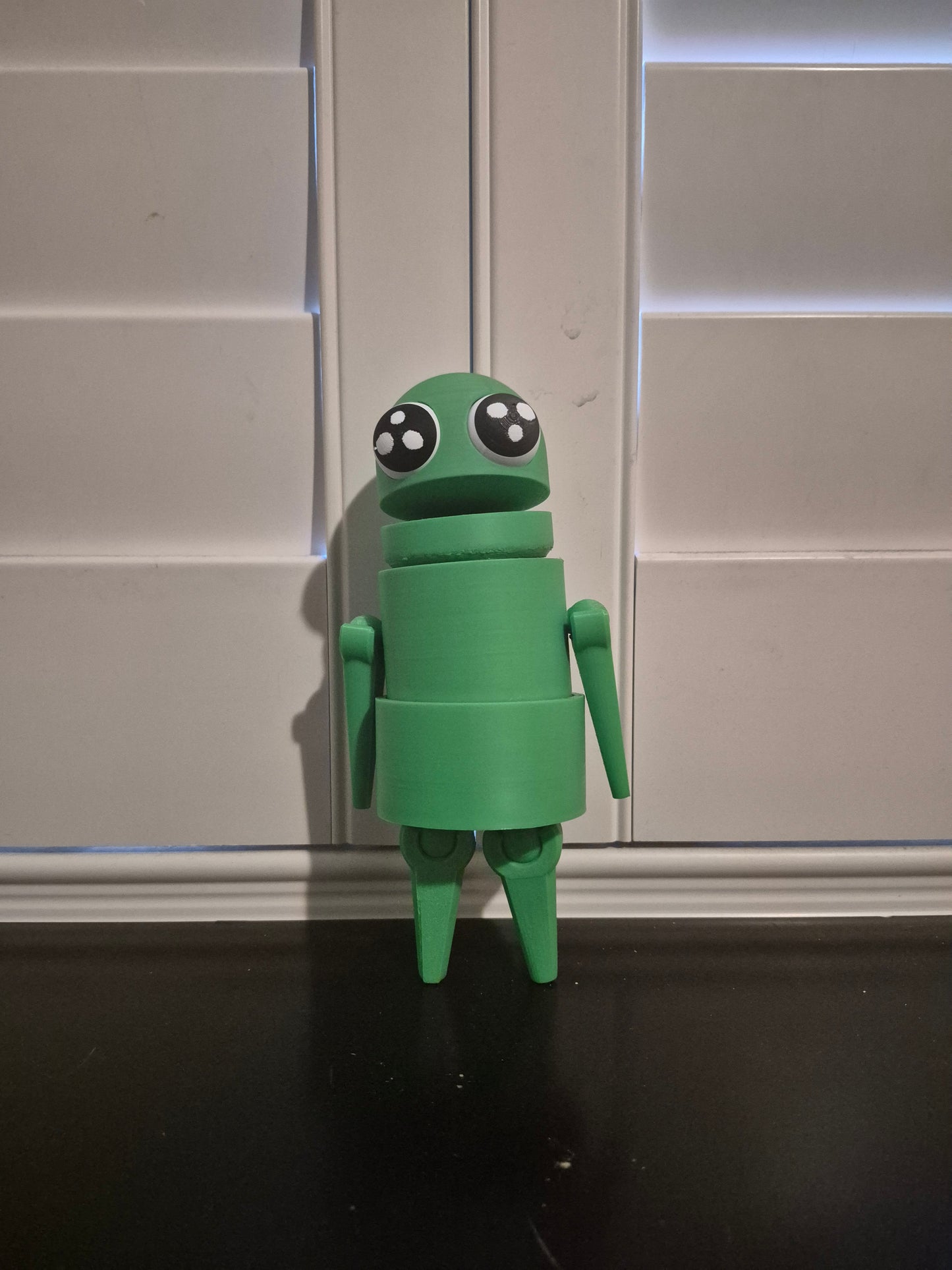 Green plastic robot figurine with large expressive eyes standing on black surface
