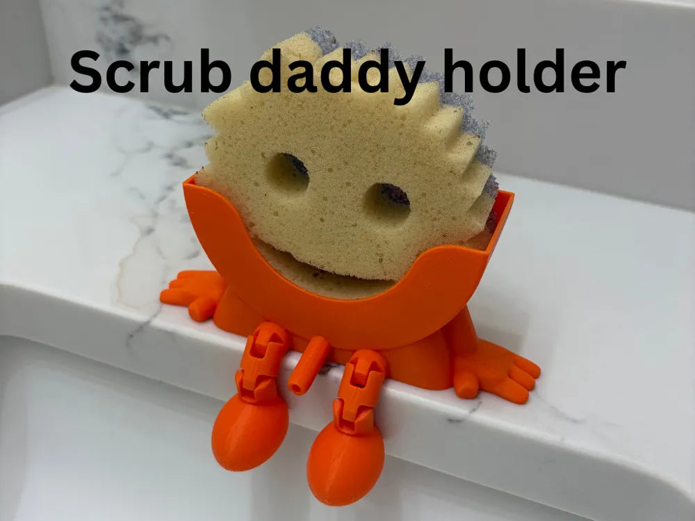 Bright orange Scrub Daddy sponge holder with flexible legs holding a sponge on a white countertop